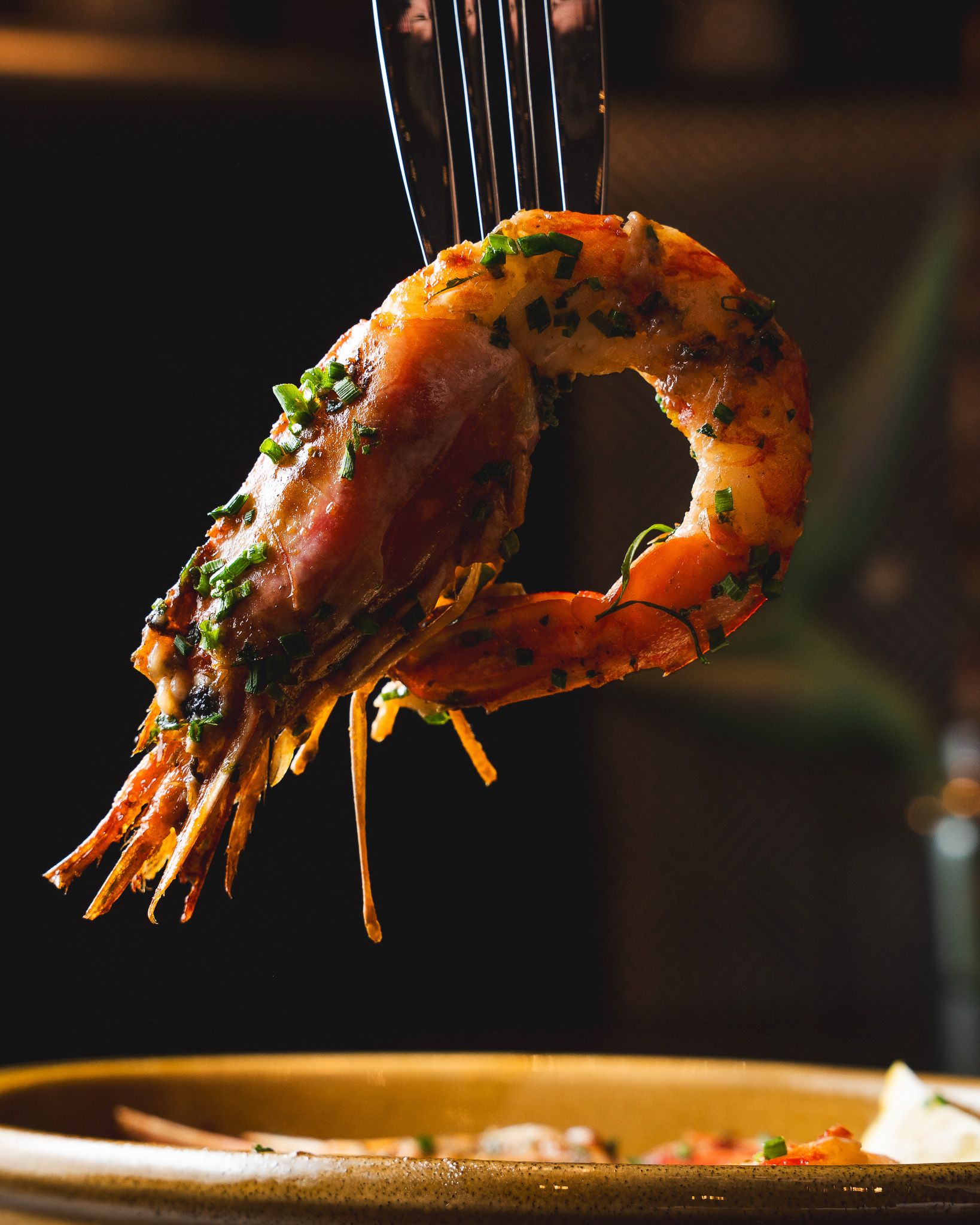 A diner lifting a prawn from a vibrant shared dish